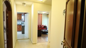 A hallway leading to a kitchen and living area with a red sofa and a coffee table. - Vino Apartment (Zalqa)