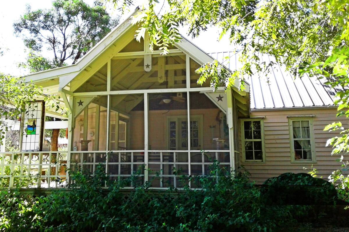 A house with a porch, a covered area with windows, and a fenced garden.