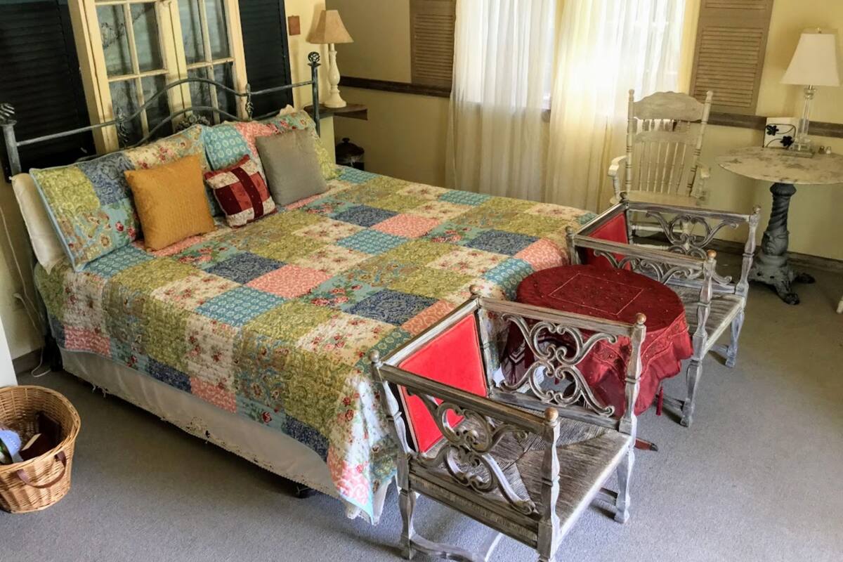 A bedroom with a bed, two chairs, a small table, and a window with curtains.