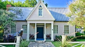 A two-story house with a gabled roof, a front porch with chairs, and a stone pathway leading to the door. - The Baines House Inn (Salado)
