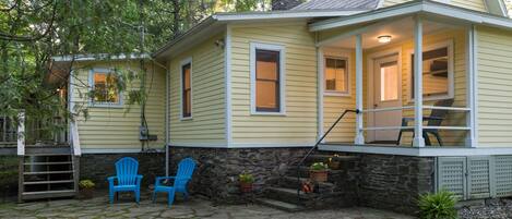 A yellow house with a stone foundation, a porch with blue chairs, and a stone staircase leading to the entrance.