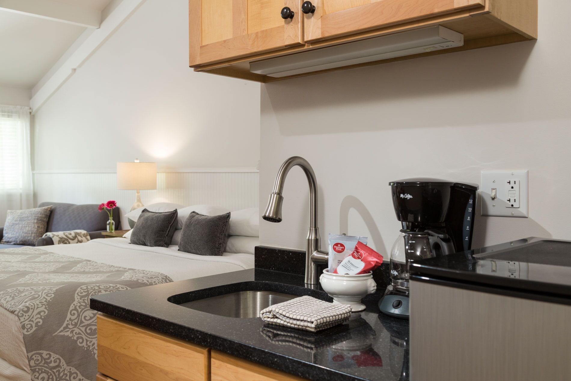 Eine kleine Küchenzeile mit Spüle, Kaffeemaschine und einem Schrank über der Arbeitsplatte.