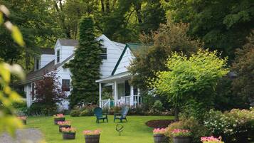 A white house with a porch, surrounded by a well-maintained garden with potted plants and flowers.