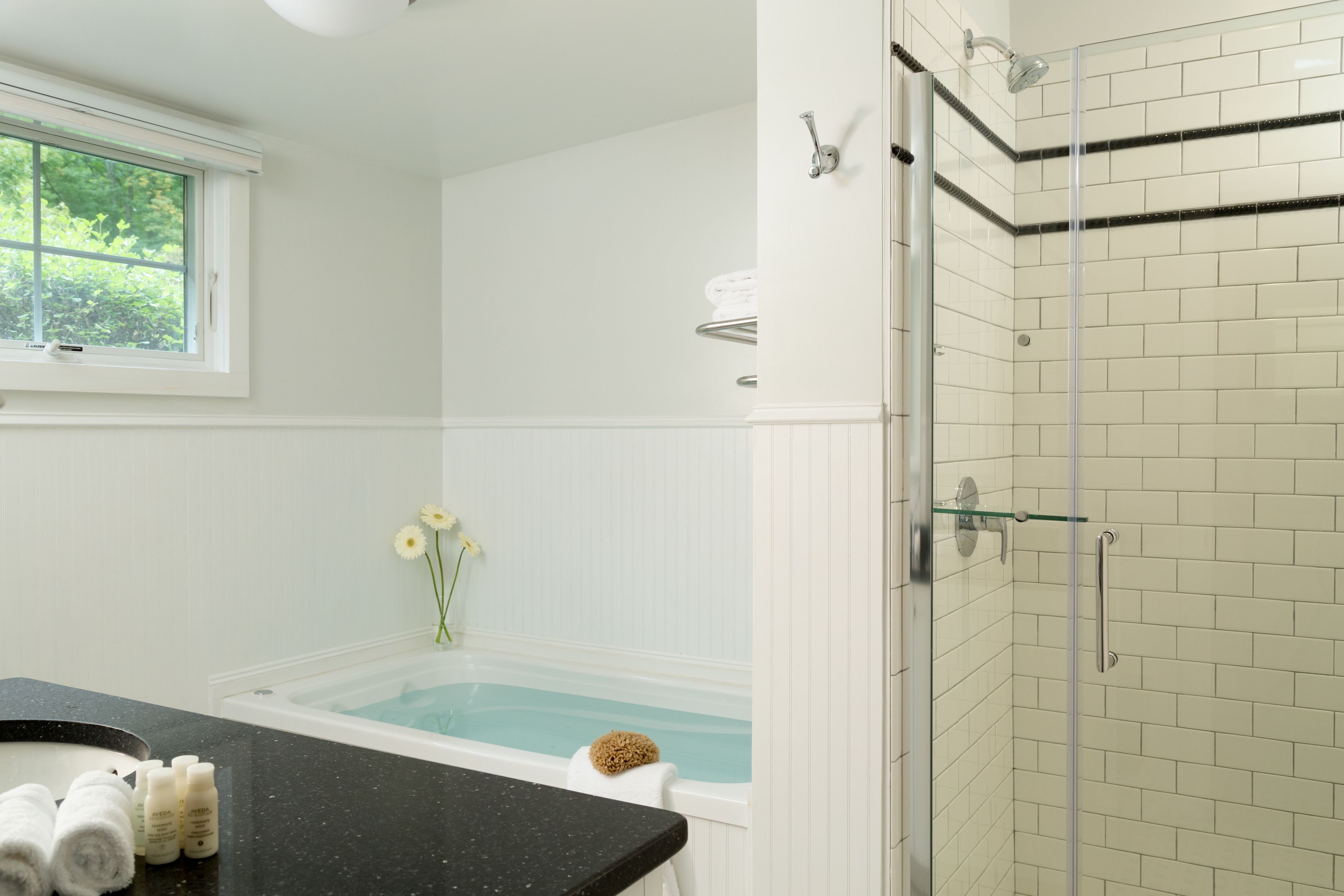 A modern bathroom with a bathtub, a glass-enclosed shower, and a window providing natural light.