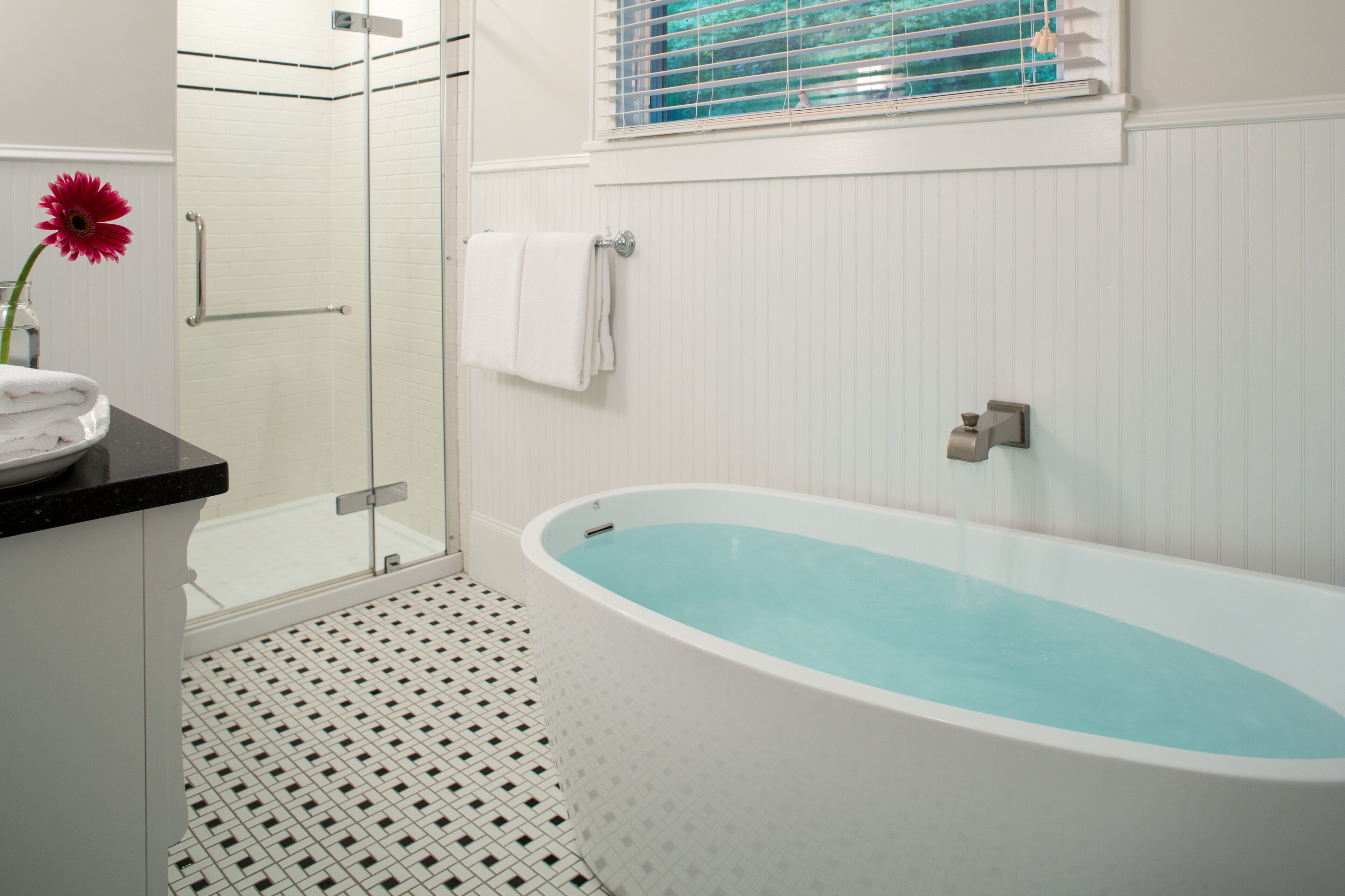 A bathroom with a freestanding bathtub, a glass shower enclosure, and a window with blinds.