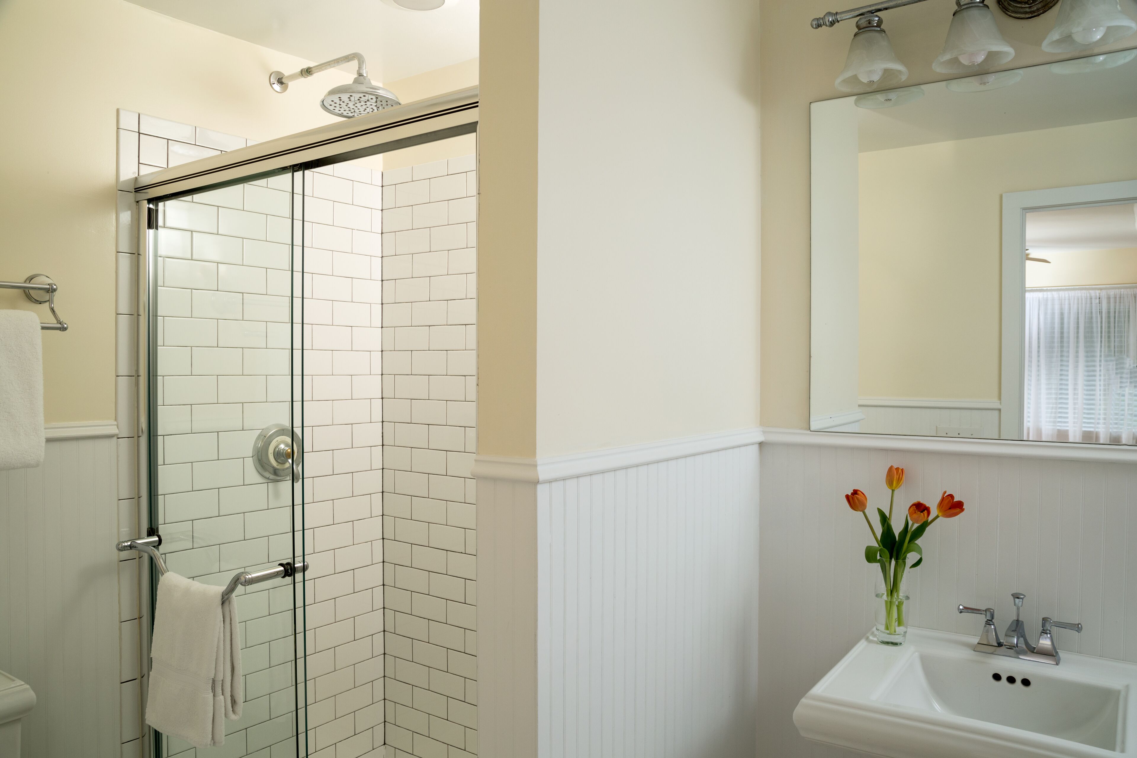 A bathroom with a glass-enclosed shower, a white sink, and a mirror above it.