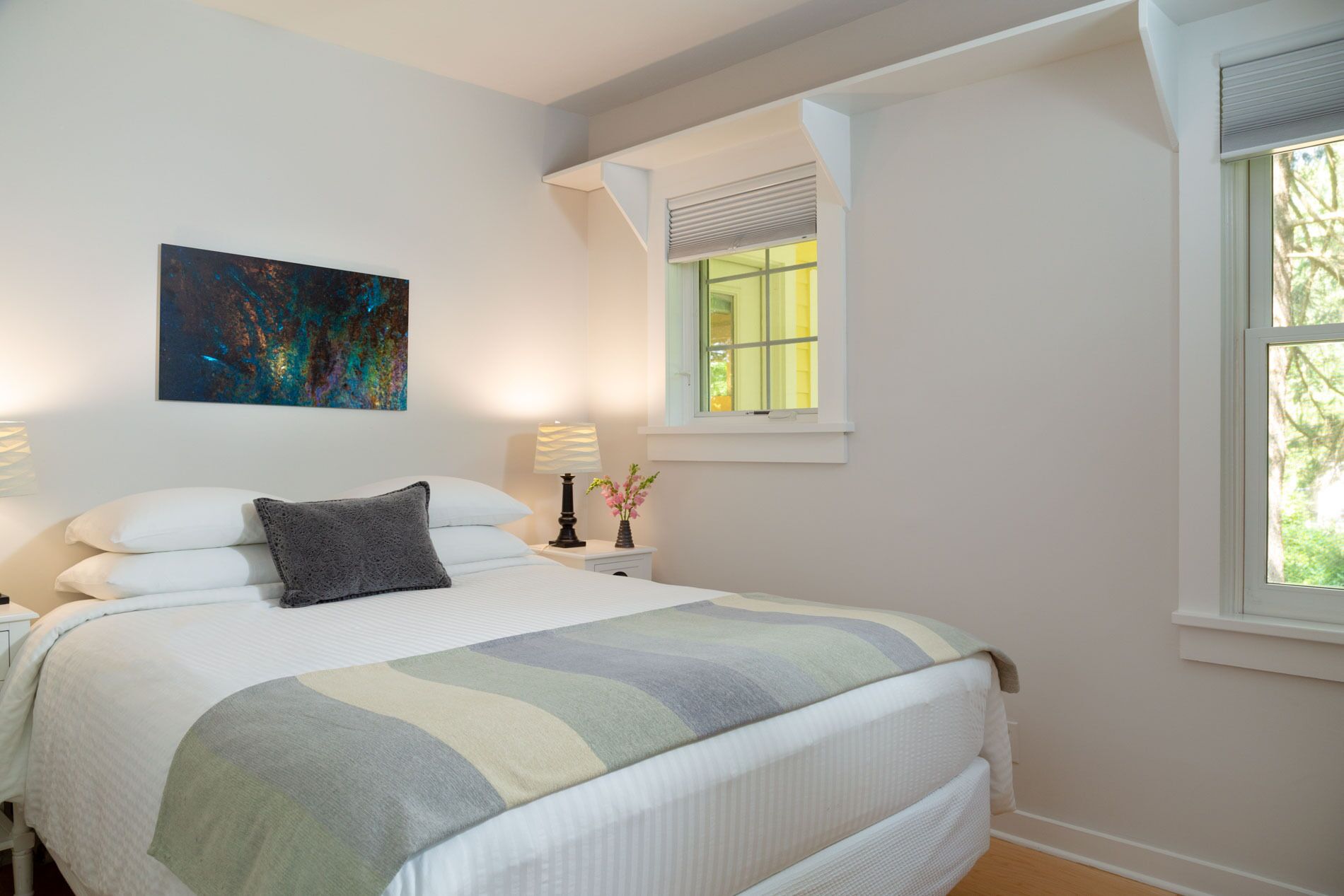 A bedroom with a bed, two bedside tables, a window, and a painting on the wall.