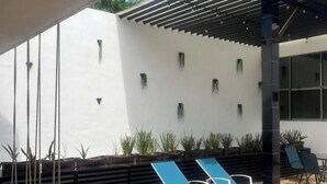 A modern outdoor lounge area with blue sun loungers, a wooden deck, and a white wall with green planters. - Casa Balam Cancun (Cancun)