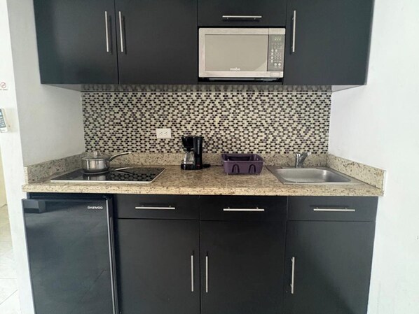 Una cocina compacta equipada con microondas, cafetera y lavamanos.