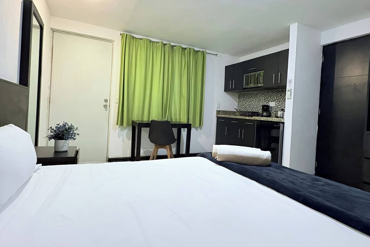 Habitación de hotel con cama, escritorio, silla, una pequeña mesa con una planta y un rincón americano.
