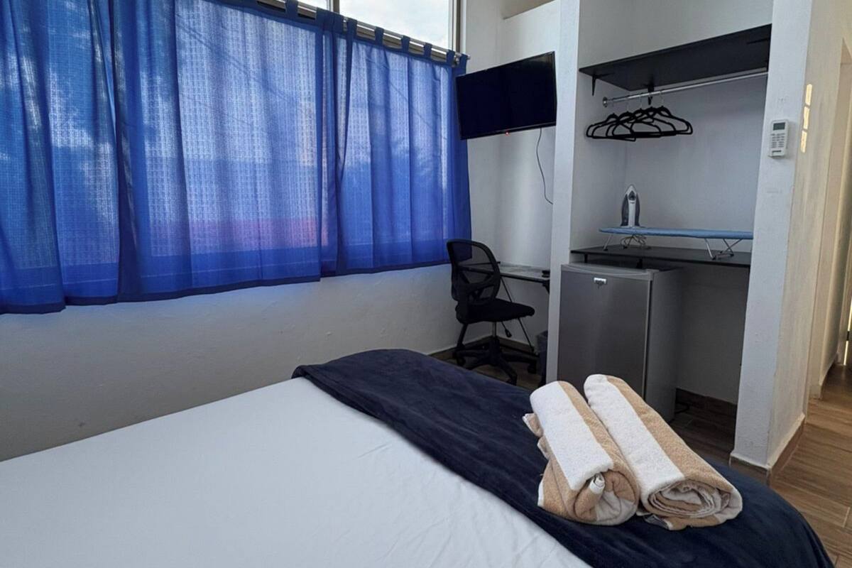Una habitación de hotel con cama, escritorio y una pequeña kitchenette.