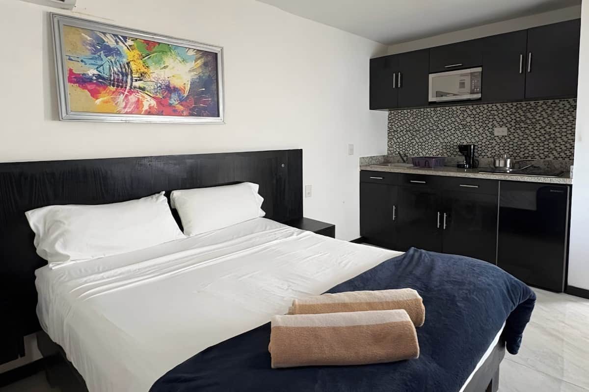Habitación de hotel con cama, un cuadro y una kitchenette con armarios y microondas.