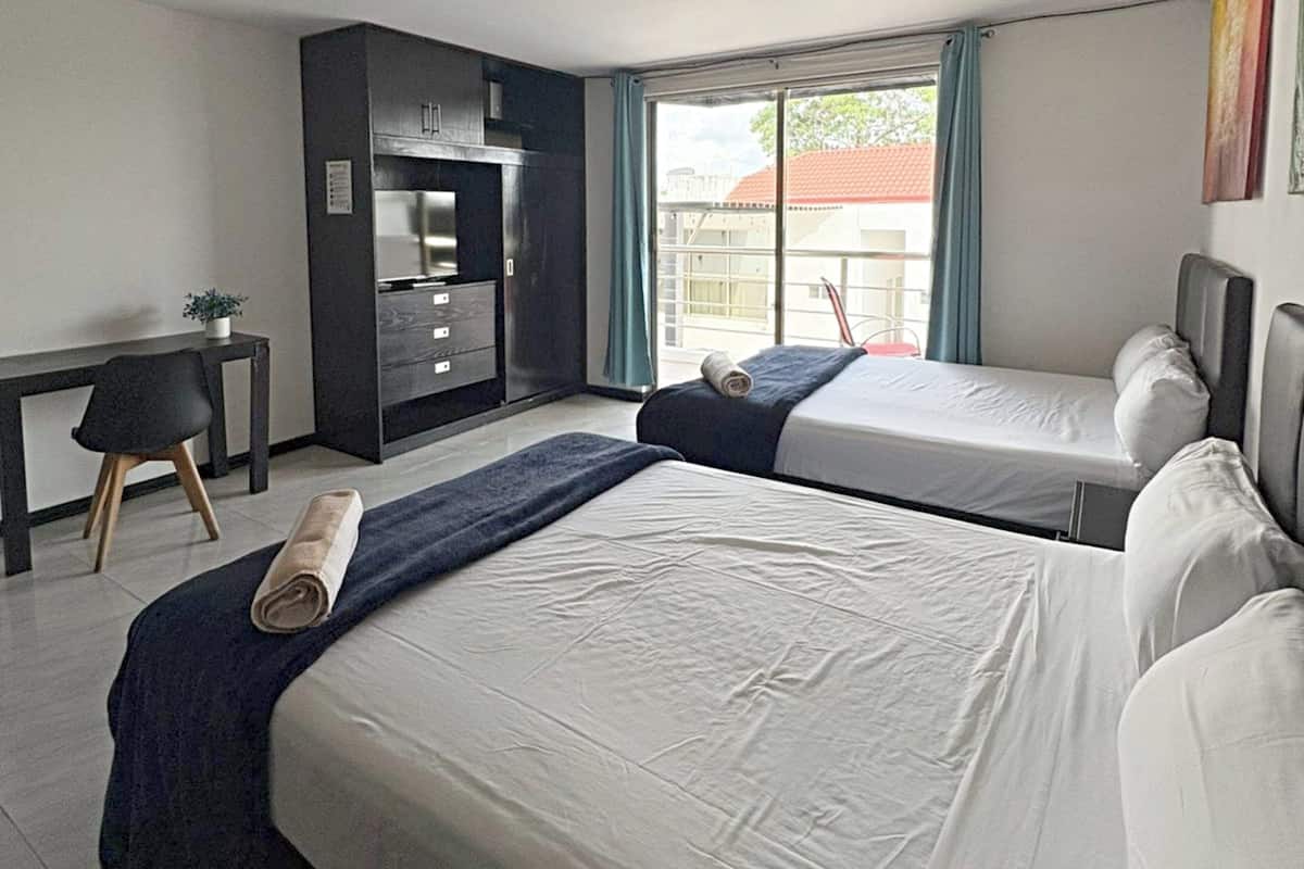 Habitación de hotel con dos camas, un escritorio, una silla y una ventana con vistas a edificios.