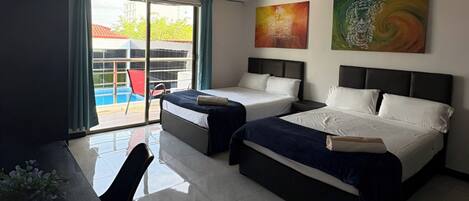 A hotel room with two beds, a desk, and a view of a swimming pool.