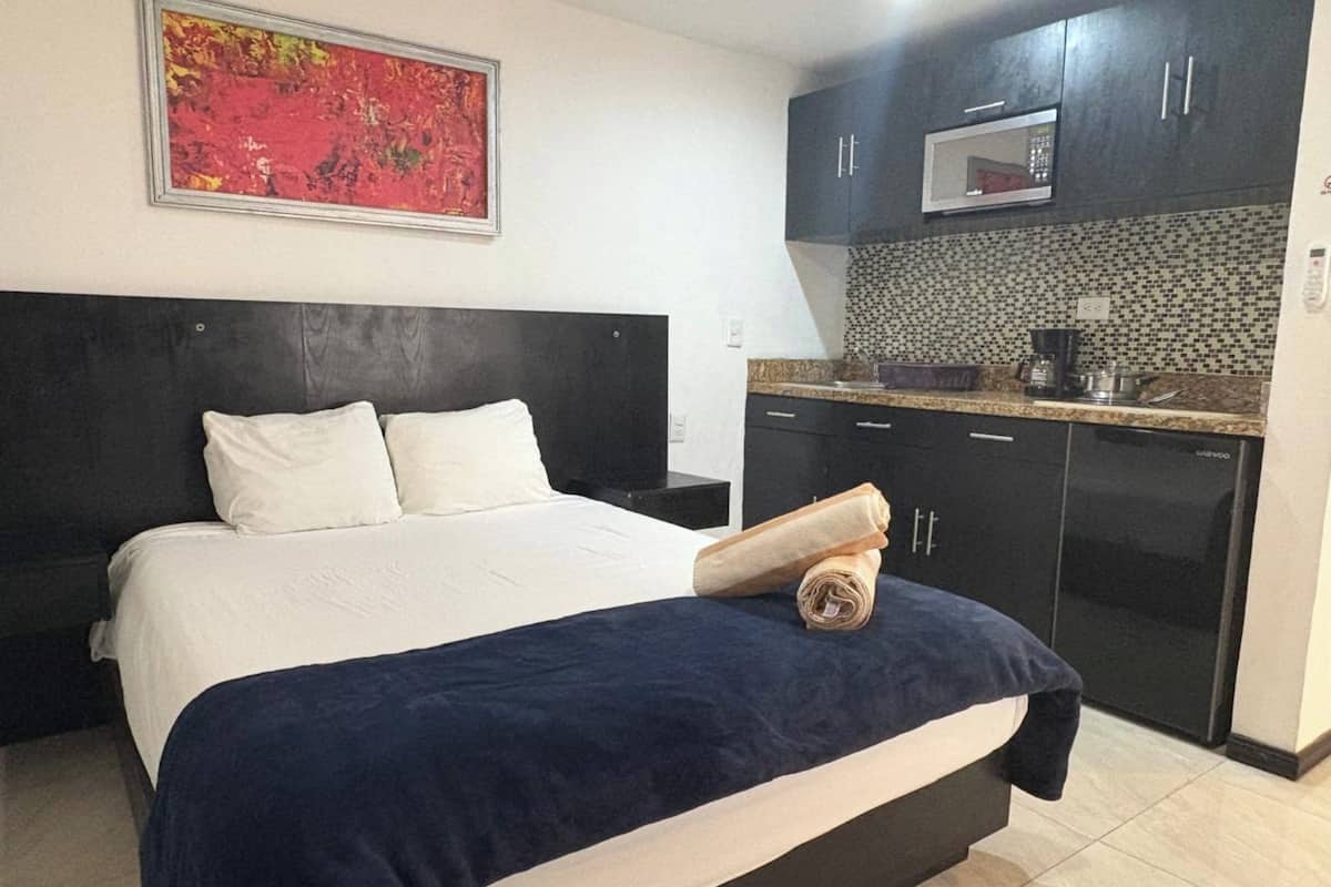 Una habitación de hotel con cama, mesita de noche, microondas, cafetera y salpicadero de azulejos.