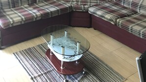 Una sala de estar con un sofá seccional, una mesa de centro de vidrio y un tapete estampado.