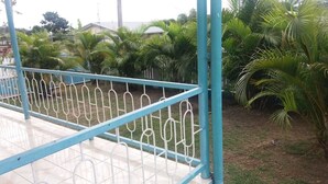 A blue metal railing with a white design, surrounded by green palm trees and a grassy area. - Two Bedroom House HHK-17-2 (Lautoka)