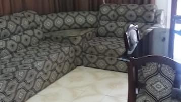 A corner living room with a patterned sofa, a wooden chair, and a tiled floor.
