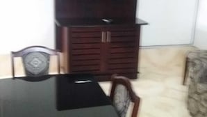 A dining area with a black table and chairs, a TV mounted on a wooden cabinet, and a patterned rug on the floor. - Two Bedroom House HHK-17-2 (Lautoka)