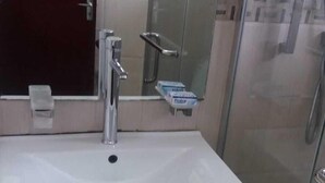 Une salle de bain avec un lavabo blanc, un miroir, une douche en verre et un meuble avec des tiroirs.