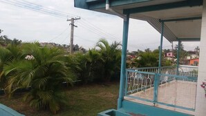Un espace extérieur abrité, doté d’une rambarde en métal, entouré de verdure et offrant une vue sur un quartier résidentiel en arrière-plan.