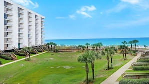 Un hotel con vista al mar, varios balcones y un césped bien cuidado con palmeras.