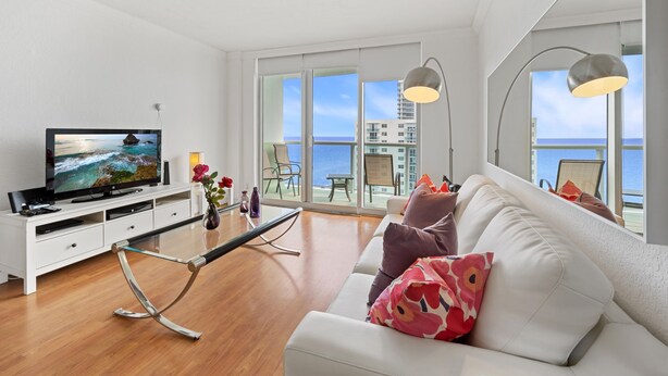 A modern living room with a television, white sofa, and large windows overlooking the sea. - 15K on the Ocean with Lateral Ocean Views (Hollywood)