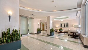 A spacious lobby with a polished marble floor, large potted plants, and a seating area with a sofa and coffee table. - 15K on the Ocean with Lateral Ocean Views (Hollywood)