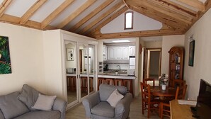 A spacious living room with a high ceiling, a sofa, a coffee table, and a dining area with wooden furniture.