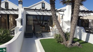 A white building with a covered patio area, outdoor seating, and palm trees.