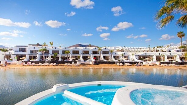 A resort with a pool, multiple white buildings, and a clear blue sky.