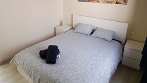 A bedroom with a bed, a ceiling fan, a painting of a beach scene, and a nightstand.