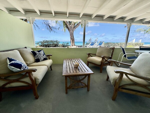 A covered outdoor seating area with a view of the ocean, wooden furniture, and a table.