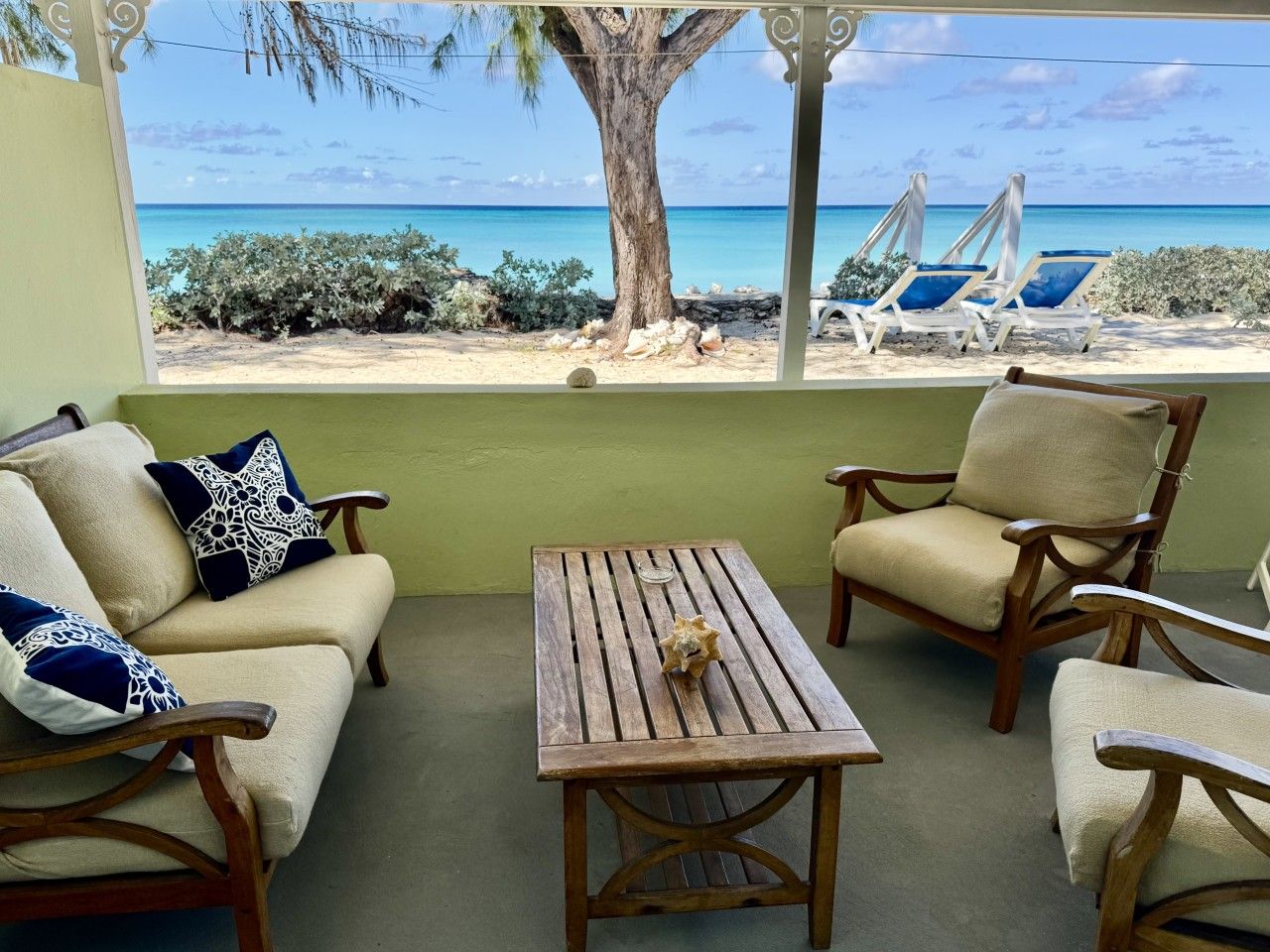 A room with a view of the beach, a wooden table, two armchairs, and a sofa with decorative pillows.