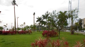 A park with green grass, red plants, and tall trees. - Relaxation and comfort on the beach - Gonzaguinha (São Vicente)