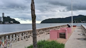 A waterfront promenade with a concrete railing, benches, and a heart-shaped sculpture. - Relaxation and comfort on the beach - Gonzaguinha (São Vicente)