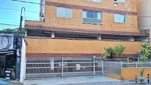 A multi-story building with a brick facade, a gated entrance, and a visible storefront on the ground floor. - Relaxation and comfort on the beach - Gonzaguinha (São Vicente)