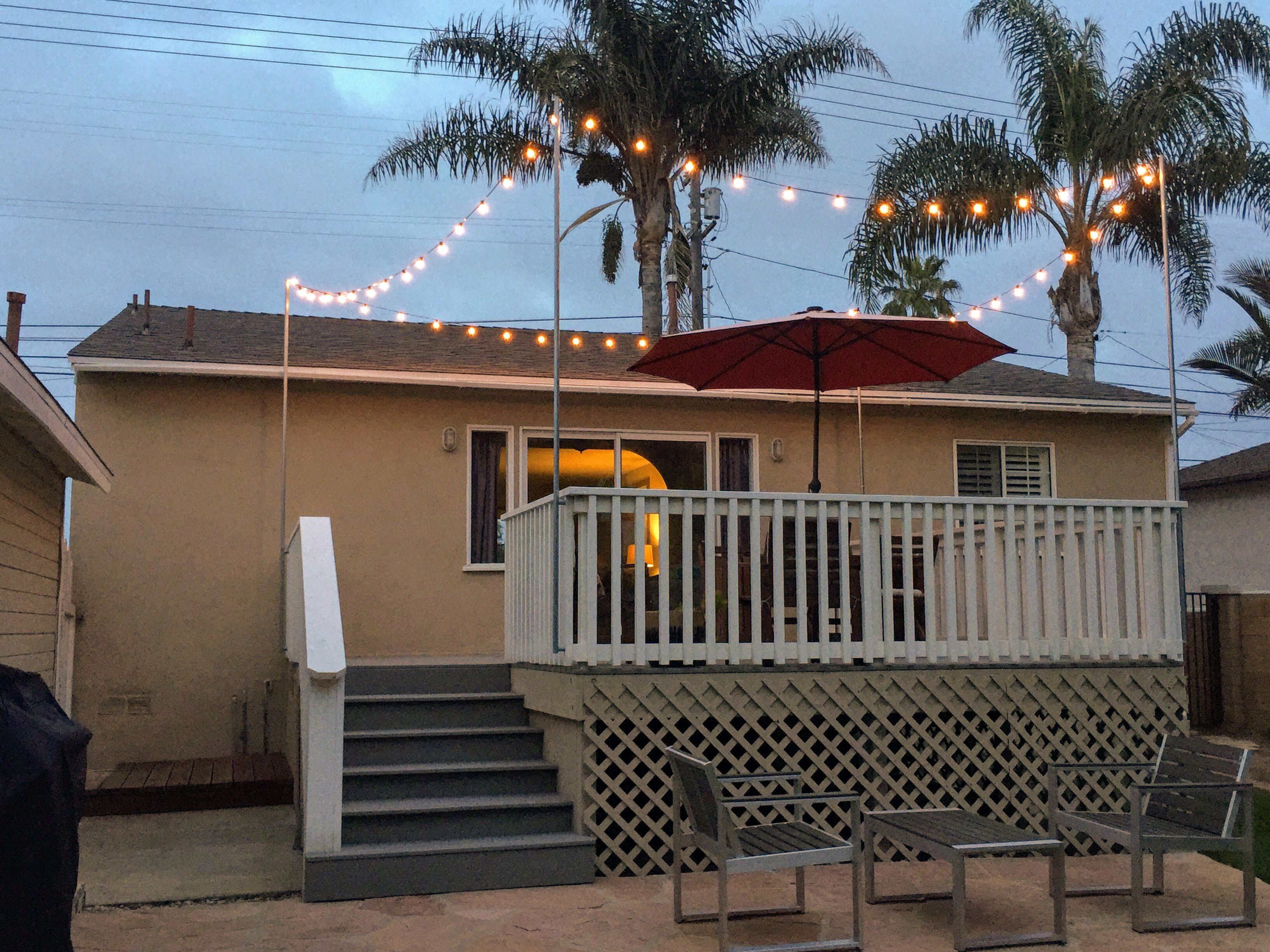A house with a balcony, a red umbrella, and string lights.