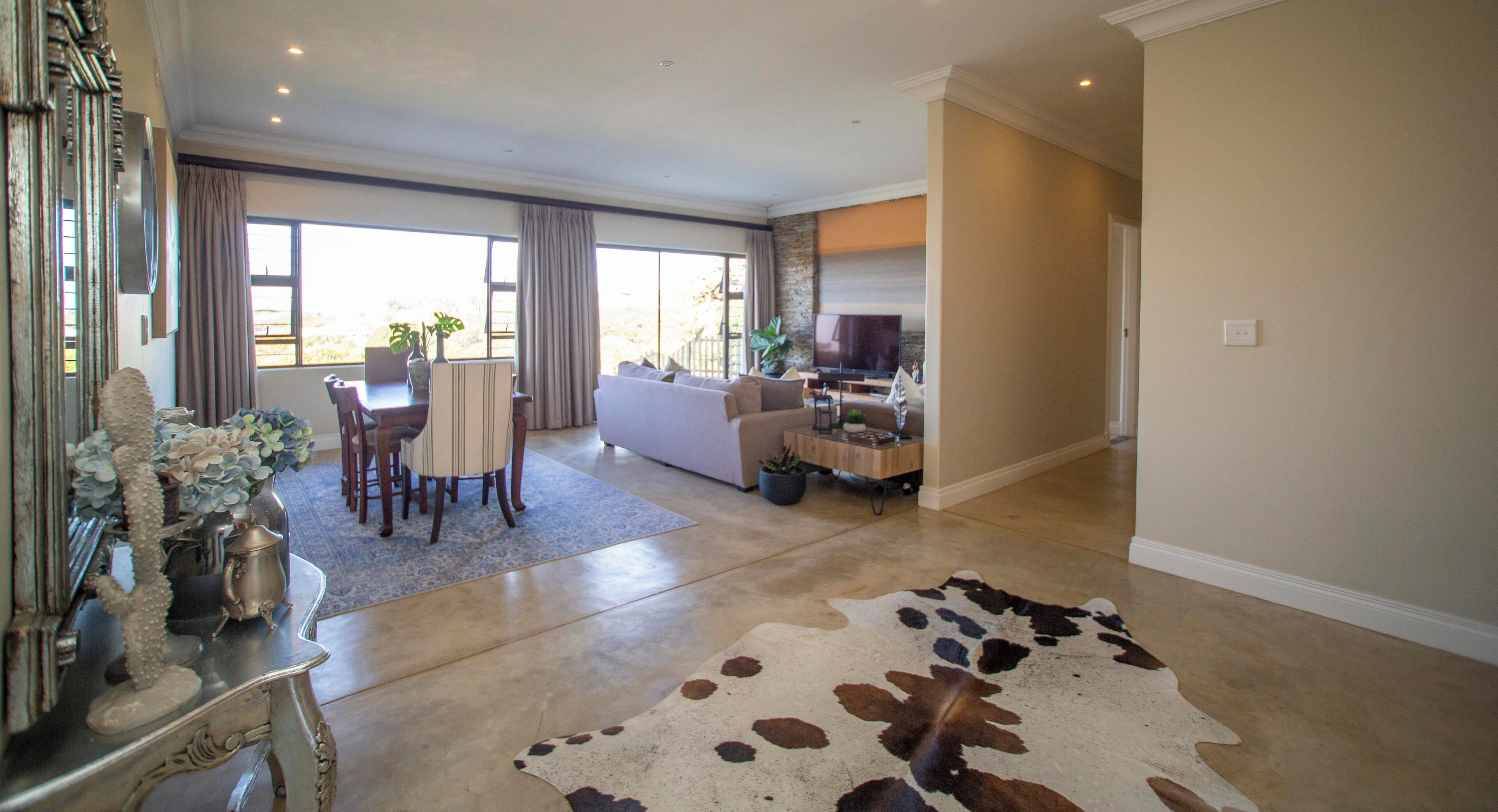 A spacious living room with a large window, a sofa, a dining area, and a flat-screen TV.