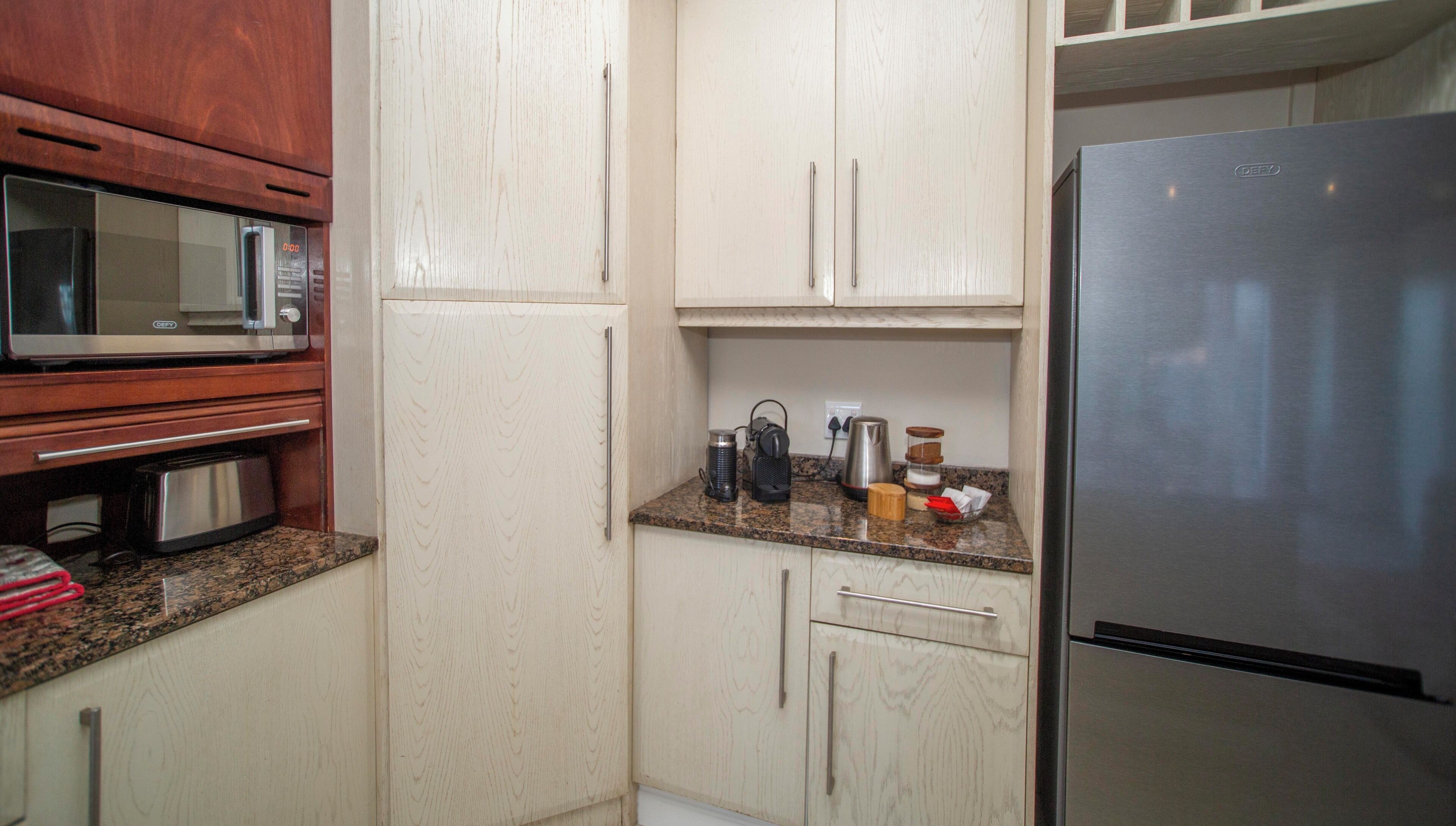 Una cocina con microondas, tostadora, refrigerador y varios utensilios de cocina sobre la encimera.