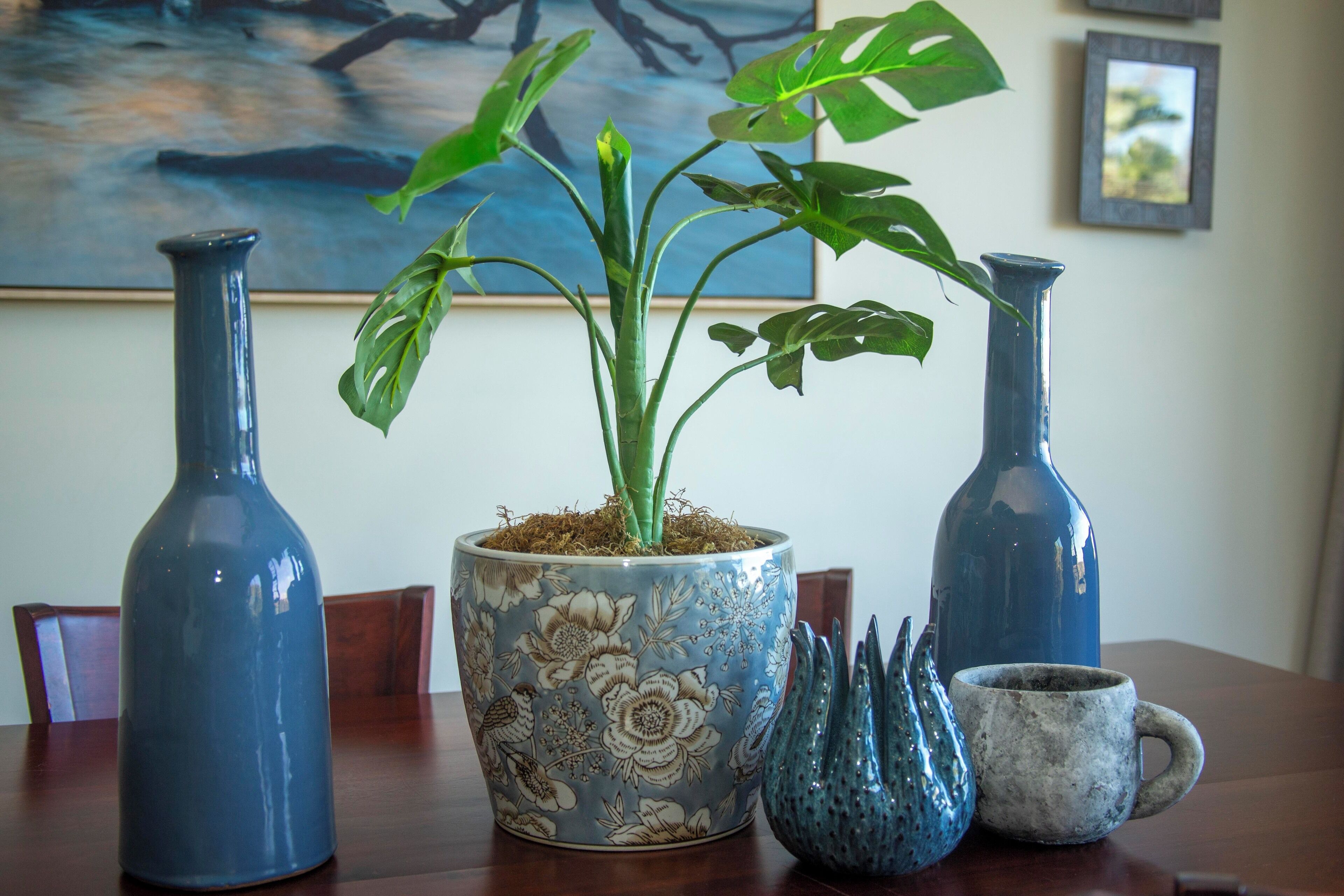 A table with a potted plant, two vases, and a mug.