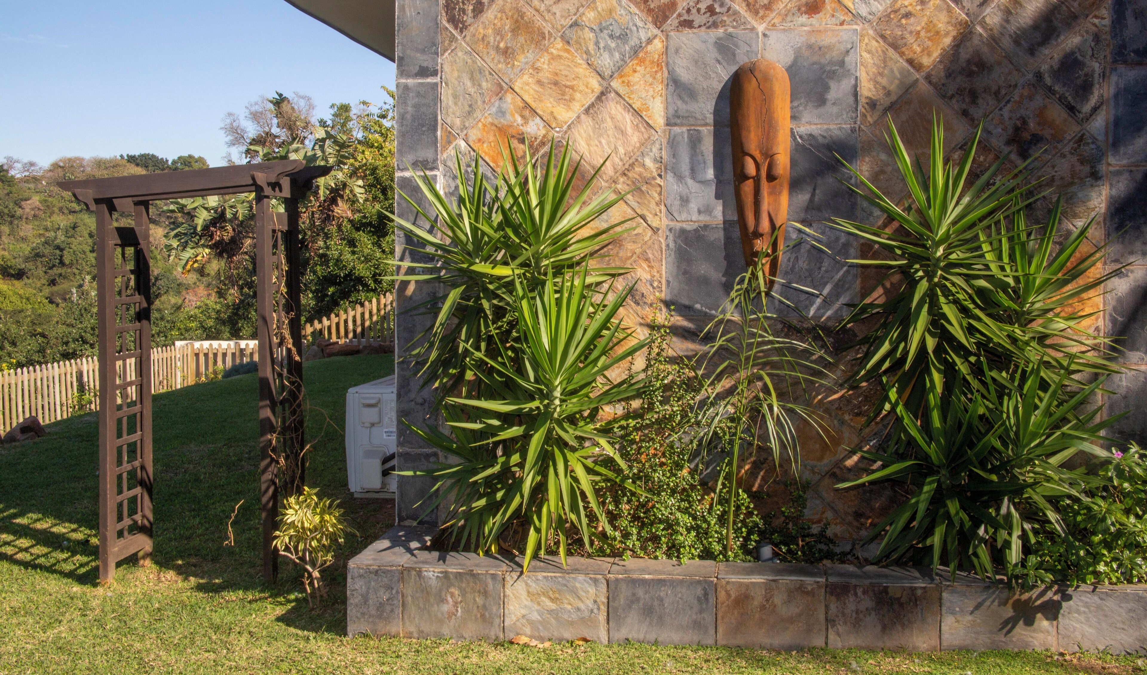 A garden area with a stone wall, a wooden pergola, and various plants.