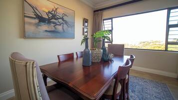 A dining area with a wooden table, chairs, a large painting, and potted plants.
