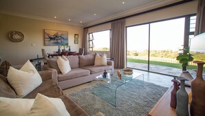 Un salón amplio con un sofá grande, una mesa de centro y vistas a un paisaje exuberante a través de amplios ventanales.