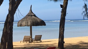 Une scène de plage avec un parasol en chaume, deux chaises longues et un objet rouge et blanc sur le sable.