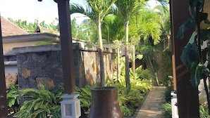 Une terrasse en bois agrémentée d’un grand vase en métal, entourée de plantes tropicales et d’un mur de pierre.