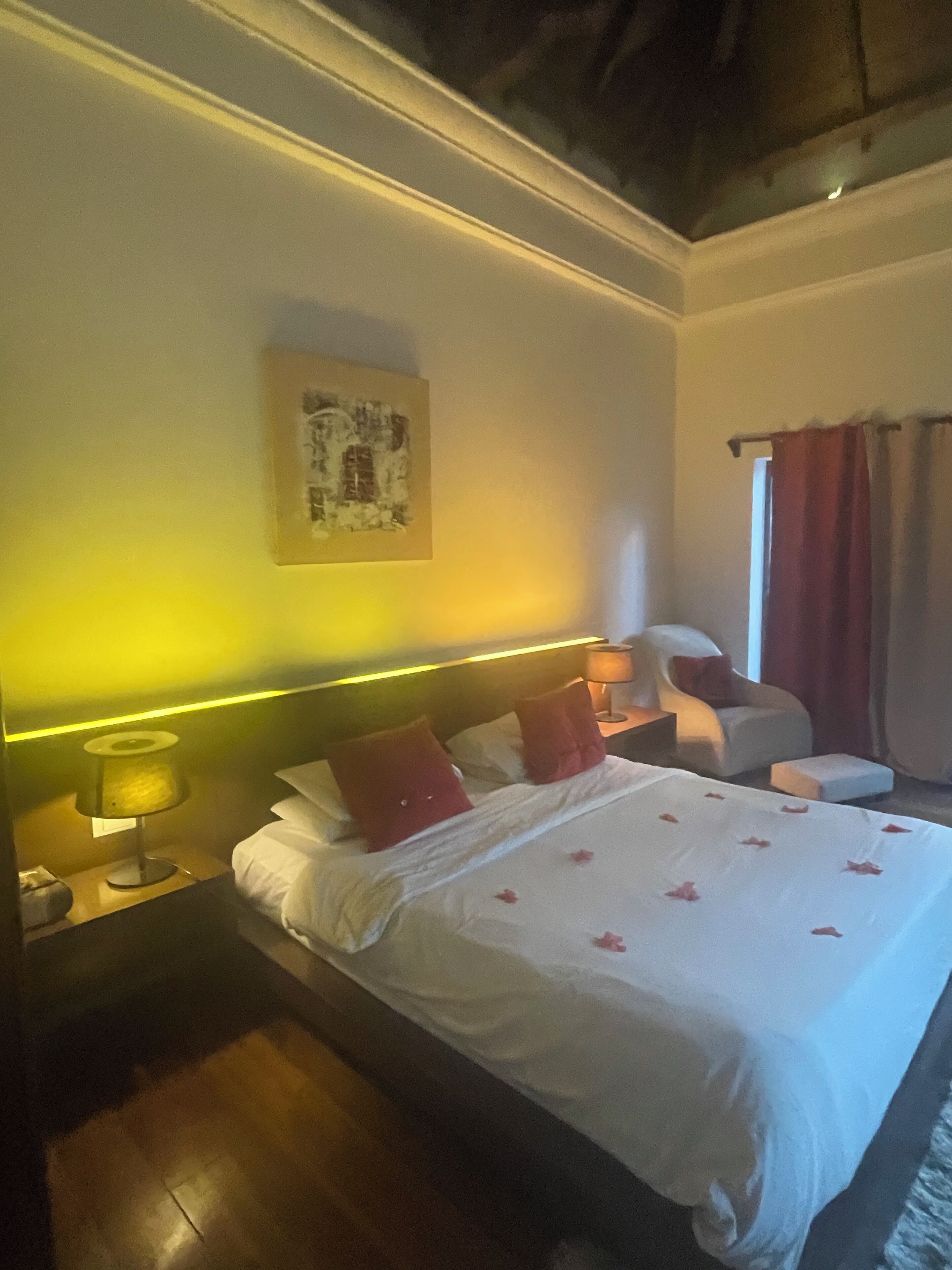 Una habitación de hotel con cama, mesita de noche, lámpara, silla y ventana con cortinas.