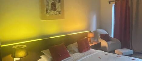 Una habitación de hotel con cama, mesita de noche, lámpara, silla y ventana con cortinas.