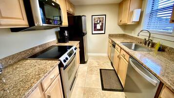 A kitchen with granite countertops, a stove, oven, microwave, refrigerator, sink, and a small rug.