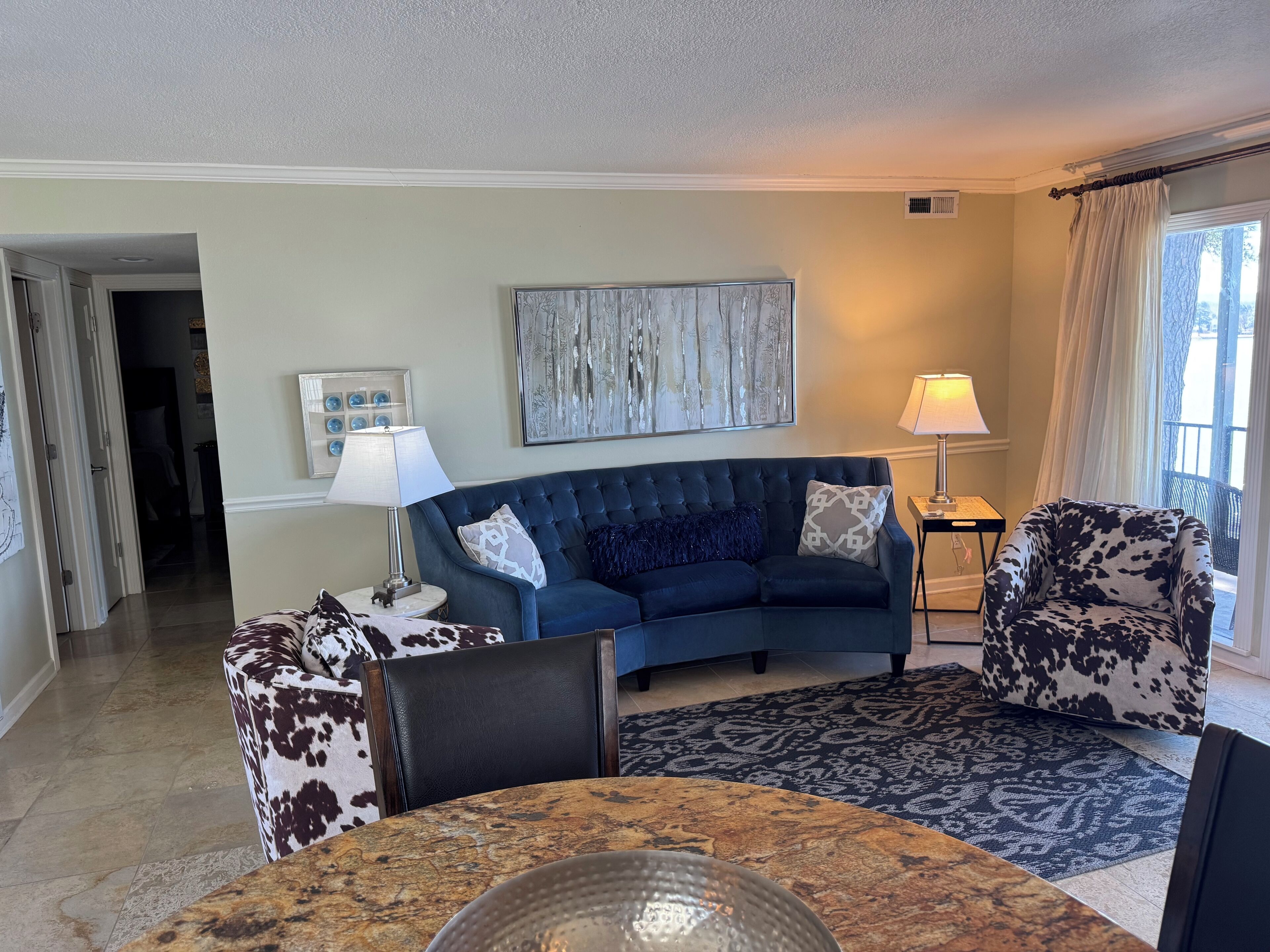A living room with a blue sofa, patterned armchairs, a coffee table, and a painting on the wall.